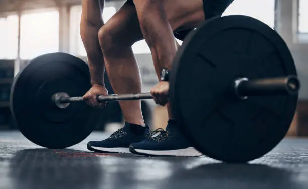 man in gym lifting a heavy barbell with black tenni shoes on lifting