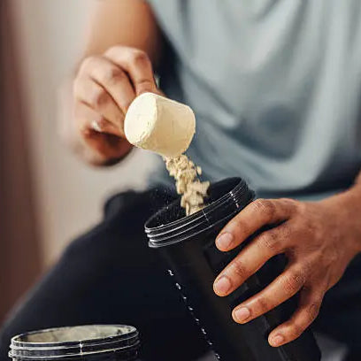 Man scooping protein powder into a cup to turn into a protein shake before working out in a grey shirt