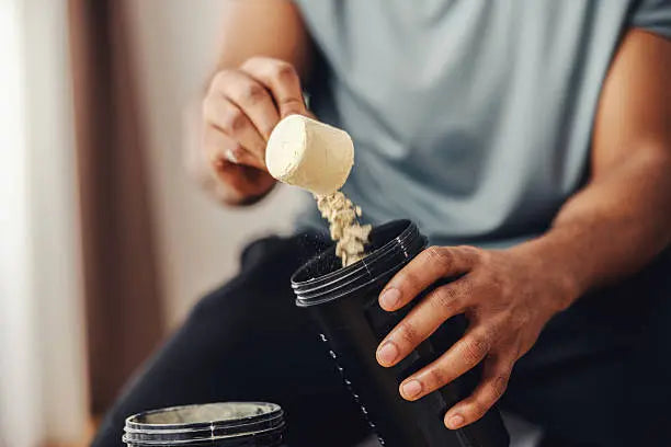 Man scooping protein powder into a cup to turn into a protein shake before working out in a grey shirt