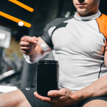Man sitting in the gym with big muscles scooping creatine getting ready to workout