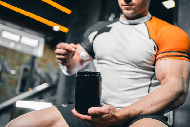 Man sitting in the gym with big muscles scooping creatine getting ready to workout