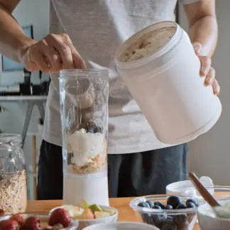 A man making a protein shake in his kitchen in a white shirt 