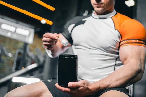 Man sitting in the gym with big muscles scooping creatine getting ready to workout