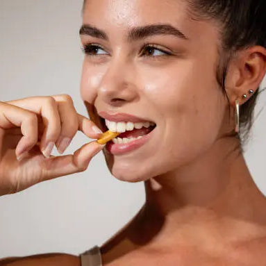 Women taking multivitamin with clear and glowing skin. She is wearing a tank top and has silver hoops in. 