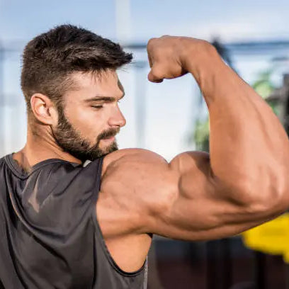 A buff man in a grey tank top flexing his bicep muscles 