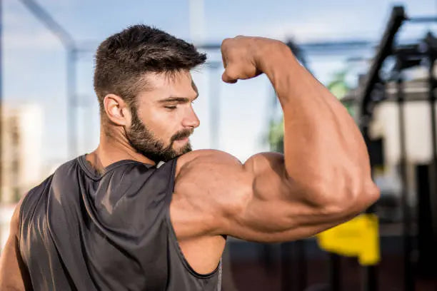 A buff man in a grey tank top flexing his bicep muscles 