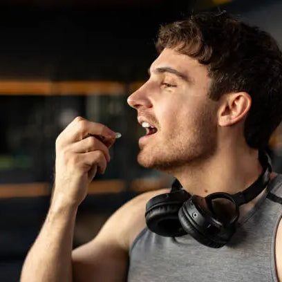 Man eating a supplement with headphones around his neck after a workout