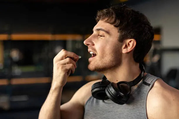 Man eating a supplement with headphones around his neck after a workout