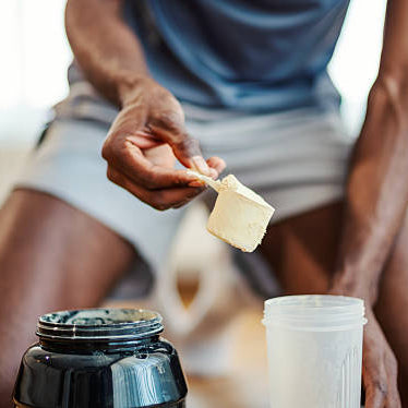 Man getting ready for gym scooping pre workout in his shaker. He is in athletic clothes.
