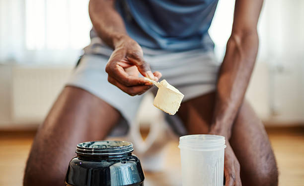 Man getting ready for gym scooping pre workout in his shaker. He is in athletic clothes.
