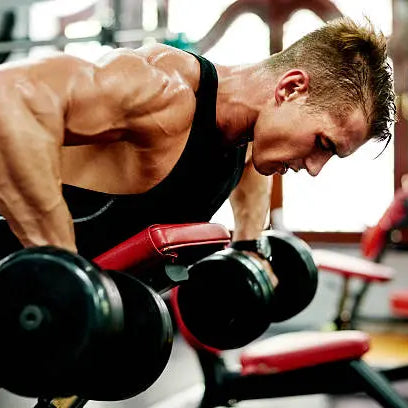 A men in the gym working out lighting heavy weights doing arm workouts on a workout bench in a black tank