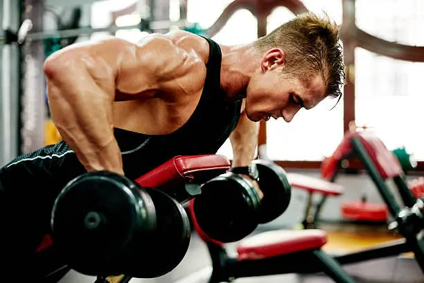 A men in the gym working out lighting heavy weights doing arm workouts on a workout bench in a black tank