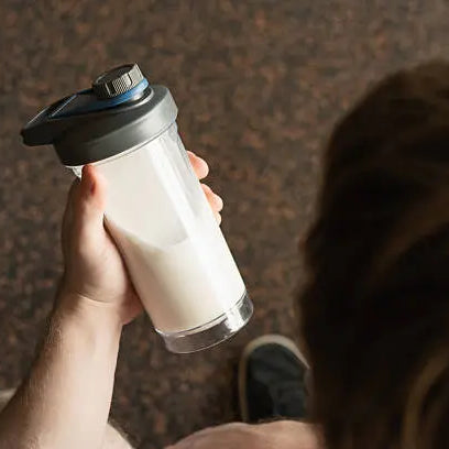 A man in workout shoes looking at his shaker that has creatine in it