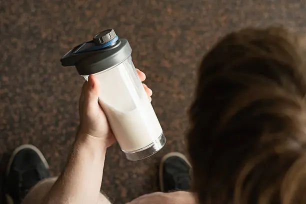 A man in workout shoes looking at his shaker that has creatine in it