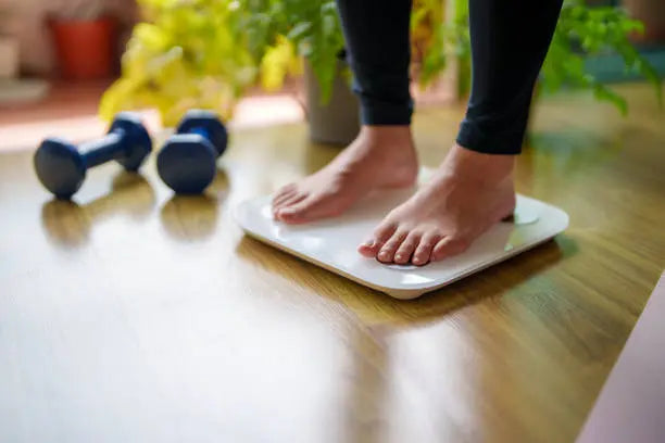 Women stepping on the scale after working out to see if she is in a weight loss plateau