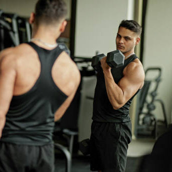 A man working out in the gym with a mirror looking at himself doing a bicep curl 