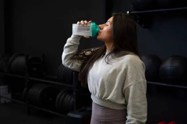 A women in the gym drinking her creatine with water 