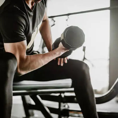A man in all black in the gym lifting weights doing arm curls building muscle 