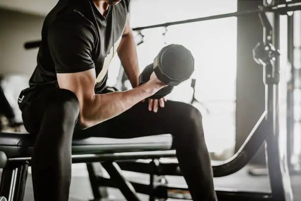 A man in all black in the gym lifting weights doing arm curls building muscle 