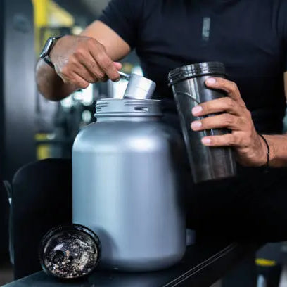 Man scooping protein powder from a grey barrel into his shaker to drink to get muscle gains